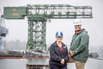 Leadership Kitsap 20 Under 40 award recipients Michelle Berger, Shop 57, Insulation Repair, Removal and Installation, and Nuclear Engineer Titus Woodson, Code 2300, Nuclear Engineering and Planning, stand in front of the iconic Hammerhead Crane at Puget Sound Naval Shipyard & Intermediate Maintenance Facility.