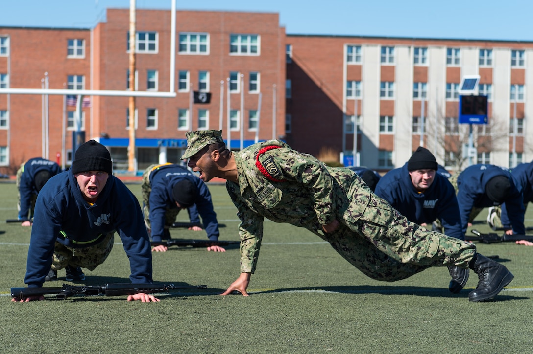 Recruit division commander assigned to Officer Training Command Newport, in Newport, Rhode Island, corrects Officer Candidate School student’s form during remedial physical training, March 9, 2020 (U.S. Navy/Darwin Lam)