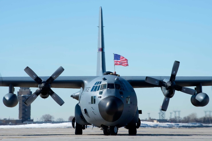 A plane on the ground with an airman holding an American flag at the top.