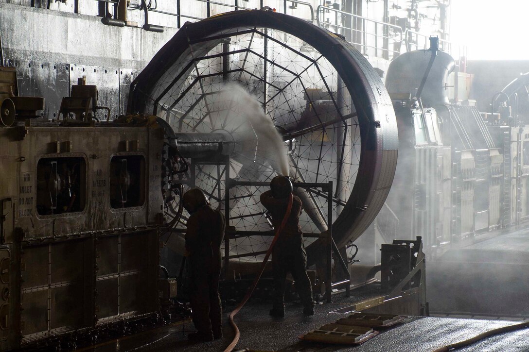 Two sailors use a hose to wash an air-cushion landing craft.