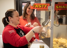 Lori Rozhon, Soldier Family Readiness Group (SFRG) leader for the 1st Theater Sustainment Command (TSC), scoops popcorn into a bag for a weekly fundraiser Feb. 27, 2020 at Fowler Hall, Fort Knox, Ky., as Theresa Scott, family readiness support assistant, 1st TSC looks on. The SFRG sells popcorn and other snacks to raise money for events for Soldiers, civilians and families of the 1TSC. (U.S. Army photo by Wendy Arevalo).