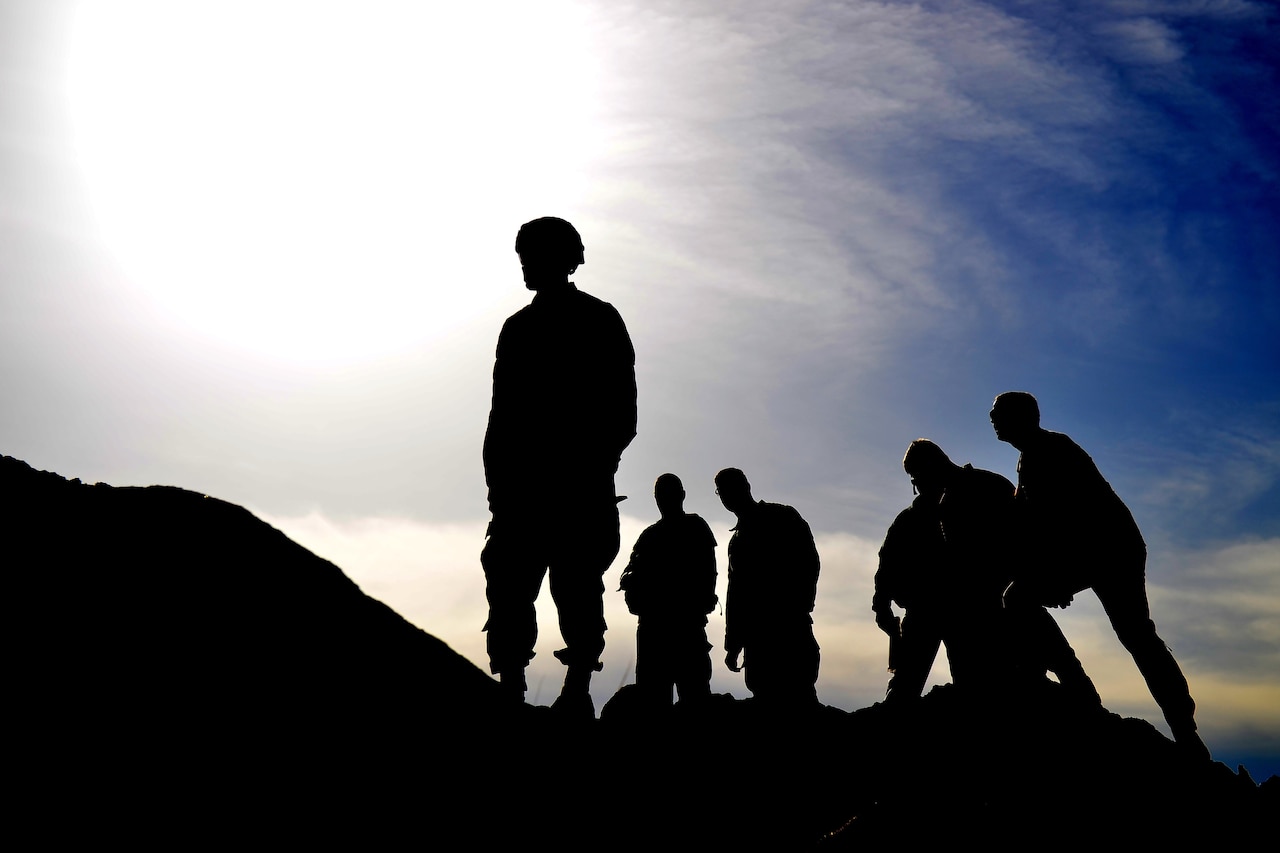 A group of soldiers stand in silhouette on a hill.