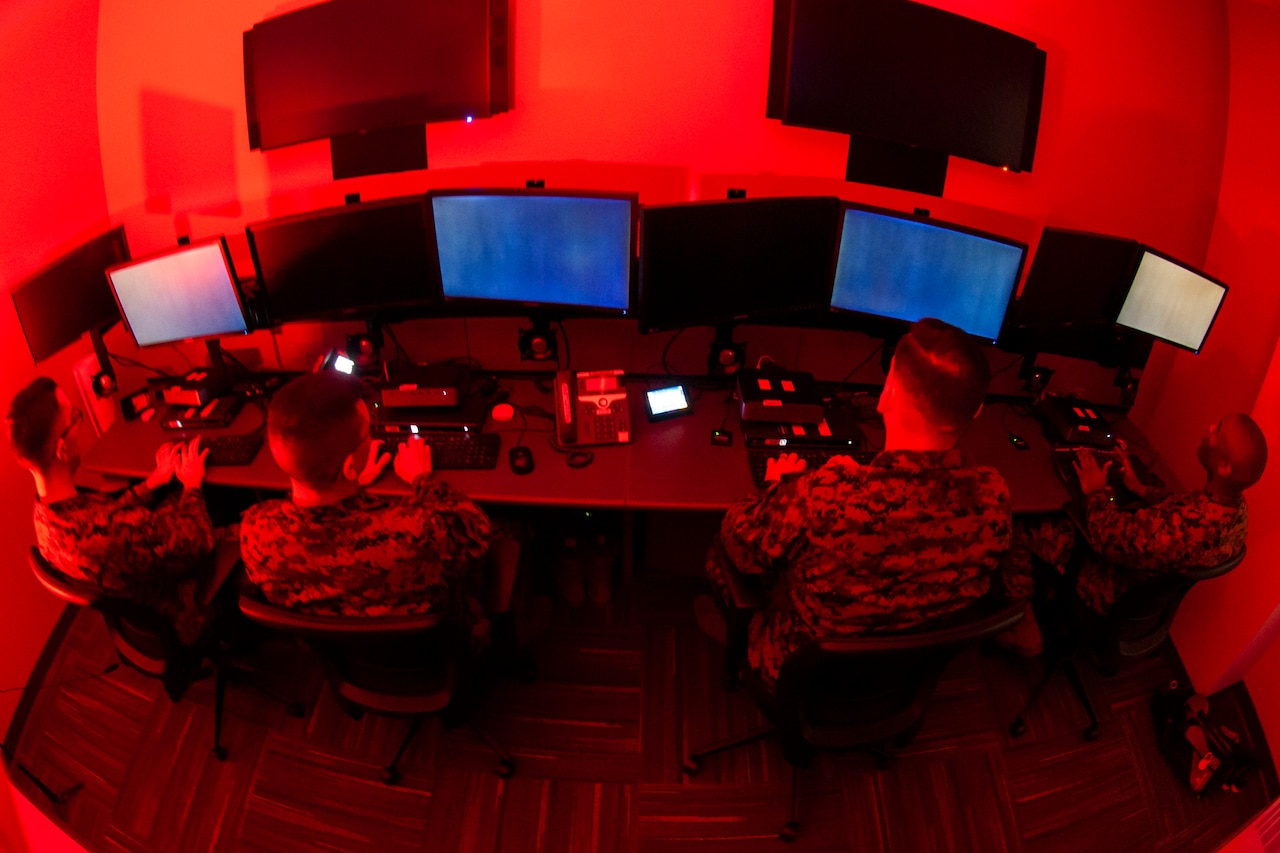 A fisheye view of three service members looking at computer monitors in what appears to be a small room.