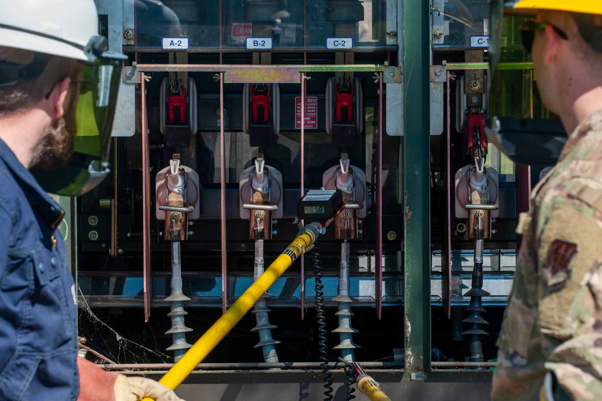 A photo of two individuals putting a high-voltage meter to a voltage distributor