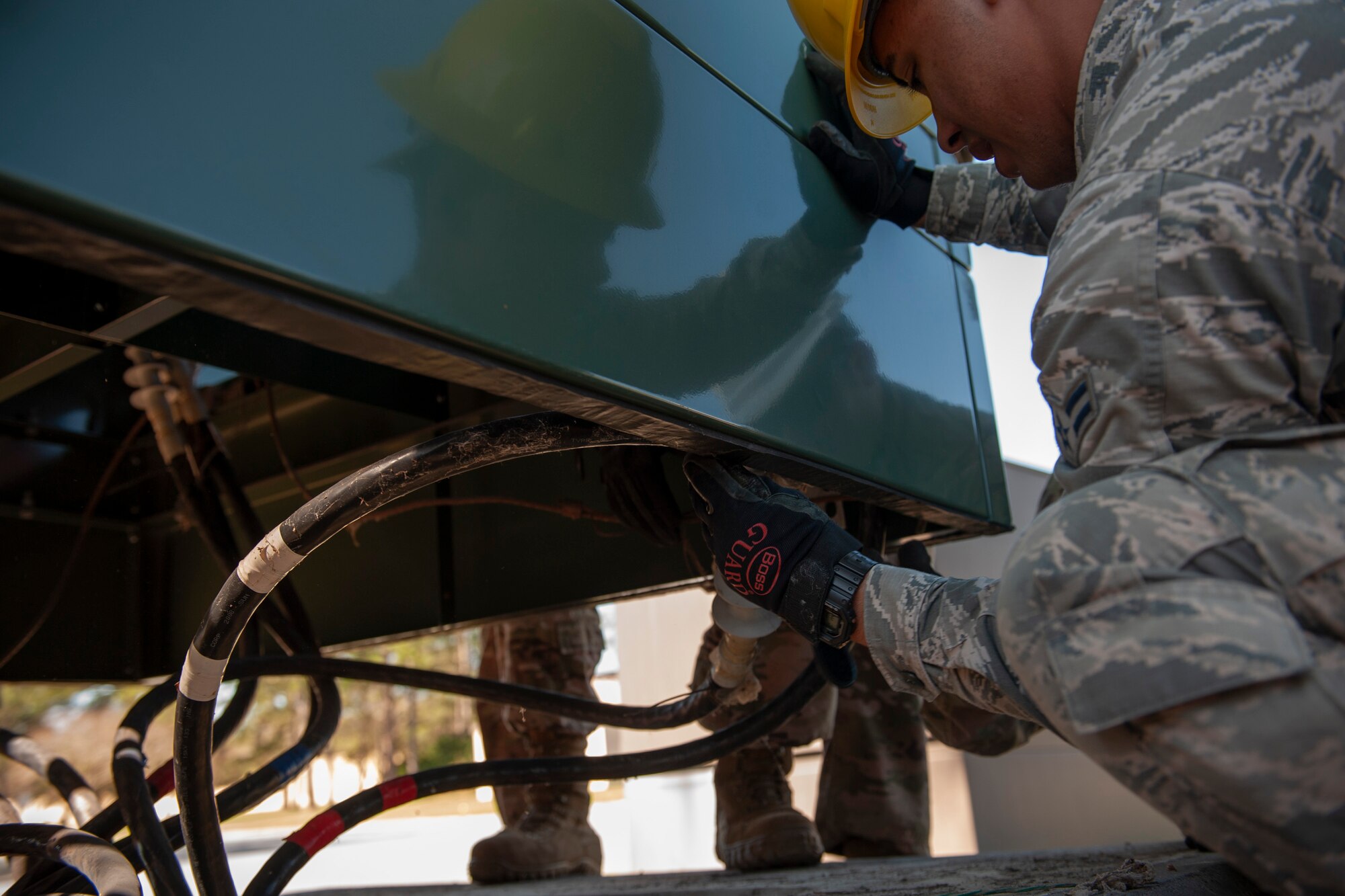 A photo of an Airman moving wire under a high-voltage distribution switch.