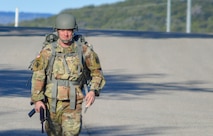 White male in green camouflage uniform and gray helmet on a road.