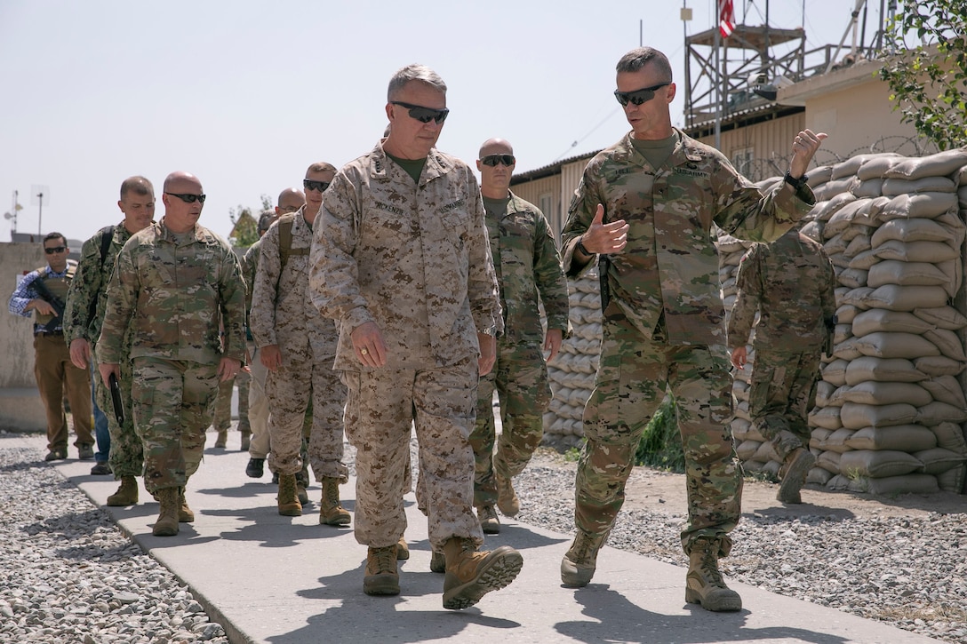 A group of military service members dressed in fatigues walk on a  sidewalk.