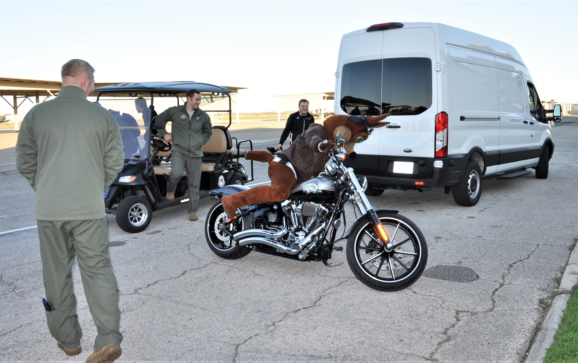 The Spurs Coyote climbs on his custom Harley on the Joint Base San Antonio-Randolph, Texas flight line February 25 where Regular Air Force, Air Force Reserve, and civilian Airmen from the 340th Flying Training Group headquarters, 39th Flying Training Squadron T-6 Texan Flight, 12th Flying Training Wing Safety, 559th Flying Training Squadron T-6 team, and 3rd Combat Camera Squadron (JBSA-Lackland) members, and the NBA San Antonio Spurs production crew worked to put the Coyote through the pilot training process. Video footage will be used for a Spurs Military Appreciation video to be shown during the March 10 game. (U.S. Air Force photo by Janis El Shabazz)