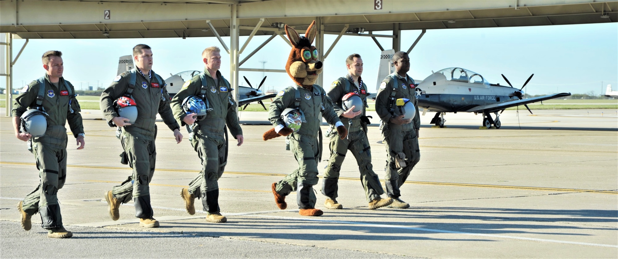The Spurs Coyote and his mission teammates for the day walk to their planes at Joint Base San Antonio-Randolph, Texas February 25 where Regular Air Force, Air Force Reserve, and civilian Airmen from the 340th Flying Training Group headquarters, 39th Flying Training Squadron T-6 Texan Flight, 12th Flying Training Wing Safety, 559th Flying Training Squadron T-6 team, and 3rd Combat Camera Squadron (JBSA-Lackland) members, and the NBA San Antonio Spurs production crew worked to put the Coyote through the pilot training process. Video footage will be used for a Spurs Military Appreciation video to be shown during the March 10 game. (U.S. Air Force photo by Debbie Gildea)