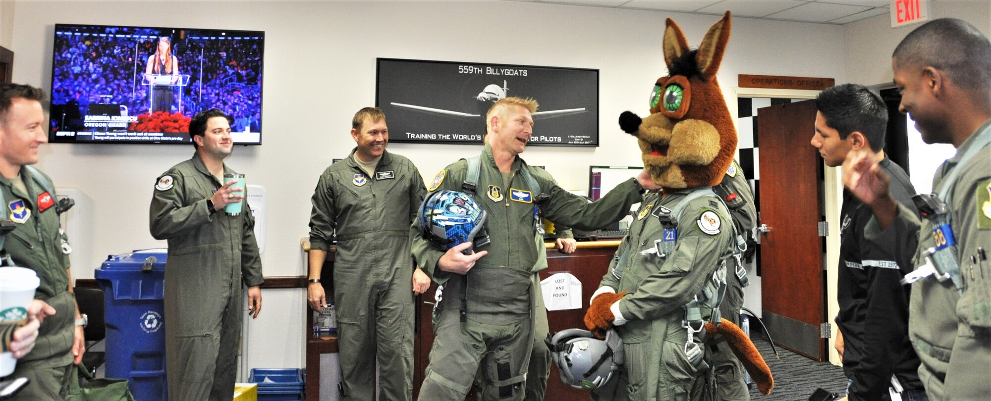 340th Flying Training Group instructor pilot – Lt. Col. Mark Pasierb (center) chats with the Spurs Coyote in the 559th Training Squadron step room February 25 following the Coyote’s simulated flight at Joint Base San Antonio-Randolph, Texas where Regular Air Force, Air Force Reserve, and civilian Airmen from the 340th Flying Training Group headquarters, 39th Flying Training Squadron T-6 Texan Flight, 12th Flying Training Wing Safety, 559th Flying Training Squadron T-6 team, and 3rd Combat Camera Squadron (JBSA-Lackland) members, and the NBA San Antonio Spurs production crew worked to put the Coyote through the pilot training process. Video footage will be used for a Spurs Military Appreciation video to be shown during the March 10 game. (U.S. Air Force photo by Janis El Shabazz)