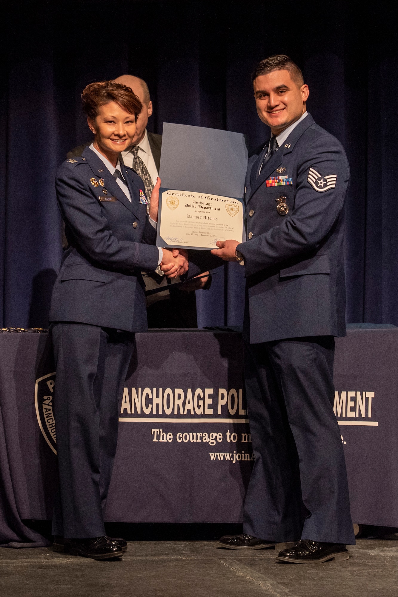 U.S. Air Force Staff Sgt. Ramses Alfonso, 673d Security Forces Squadron lead patrolman, receives a certificate of completion for graduating Anchorage Police Department 19-1 Academy from U.S. Air Force Col. Patricia Csànk, Joint Base Elmendorf-Richardson and 673d Air Base Wing commander, in Anchorage, Alaska, Dec. 5, 2019. Alfonso earned the Distinguished Honor Graduate Award, Class Valedictorian, Top Shooter, and Top Defensive Driver in the Emergency Vehicle Operations Course. The partnership between the squadron and the Anchorage Police Department provides Airmen with a clearer understanding of municipal police procedures as well as builds contacts with all partner law enforcement agencies who participate in the academy.