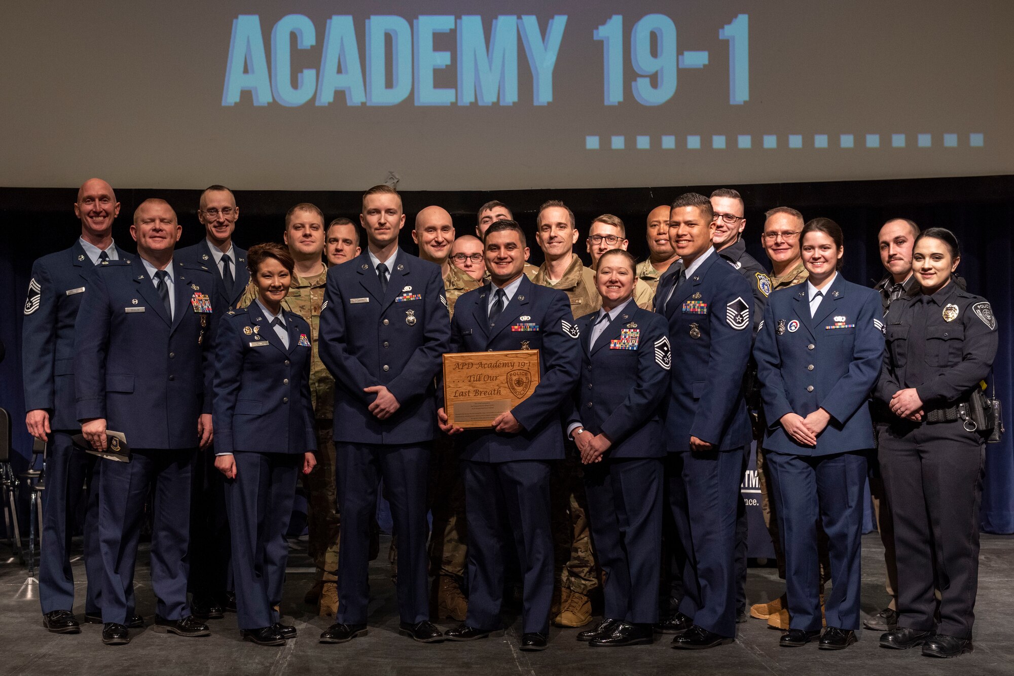 U.S. Air Force Staff Sgt. Ramses Alfonso, 673d Security Forces Squadron lead patrolman, holds an award and poses for a photo at his Anchorage Police Department 19-1 Academy graduation ceremony with base leadership and Airmen from Joint Base Elmendorf-Richardson, Alaska in Anchorage, Alaska, Dec. 5, 2019. Alfonso graduated from Anchorage Police Department 19-1 Academy and earned the Distinguished Honor Graduate Award, Class Valedictorian, Top Shooter, and Top Defensive Driver in the Emergency Vehicle Operations Course. The partnership between the squadron and the Anchorage Police Department provides Airmen with a clearer understanding of municipal police procedures as well as builds contacts with all partner law enforcement agencies who participate in the academy.