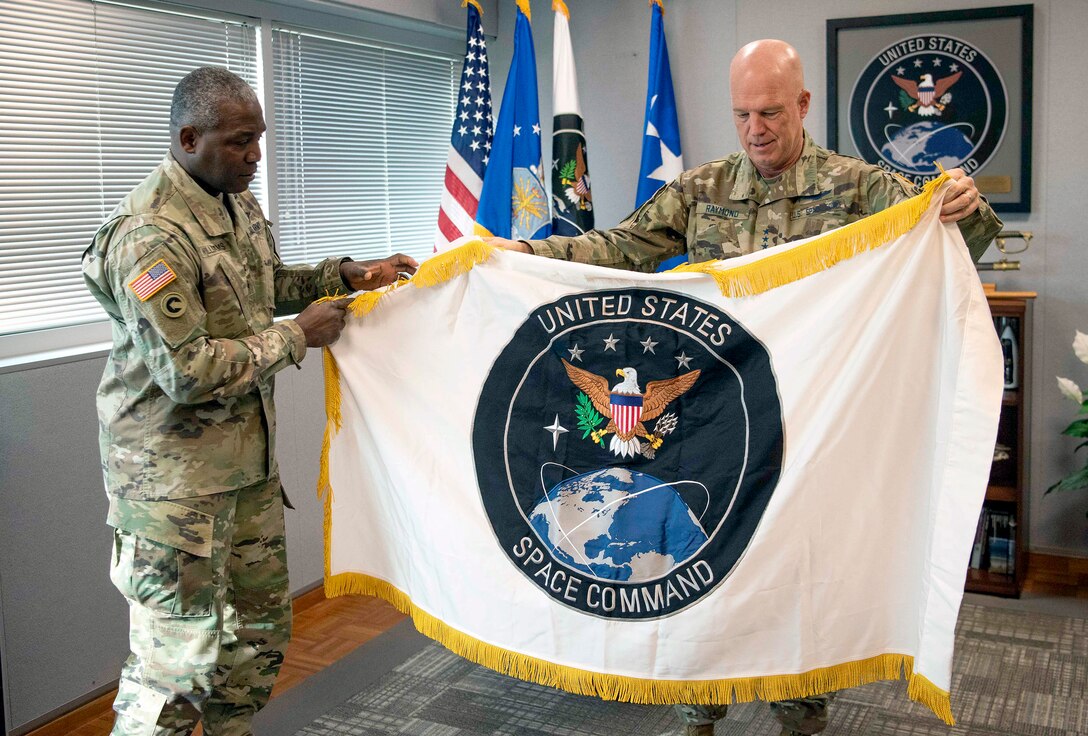 Black officer presents a large unit flag depicting the Space Command with an eagle on top of the planet Earth to a white officer.