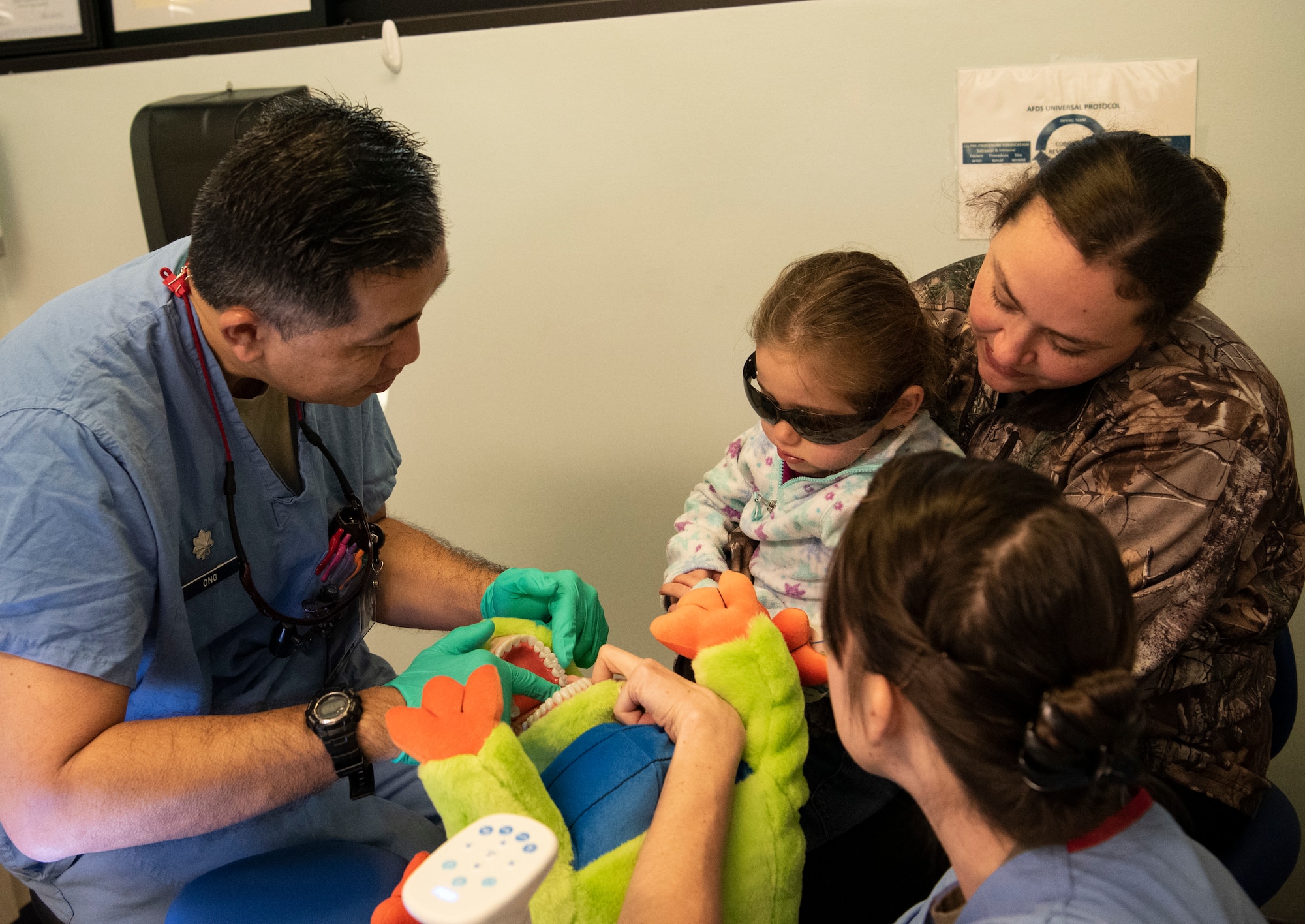 Dental clinic Airmen demonstrate to a child how they will count her teeth.