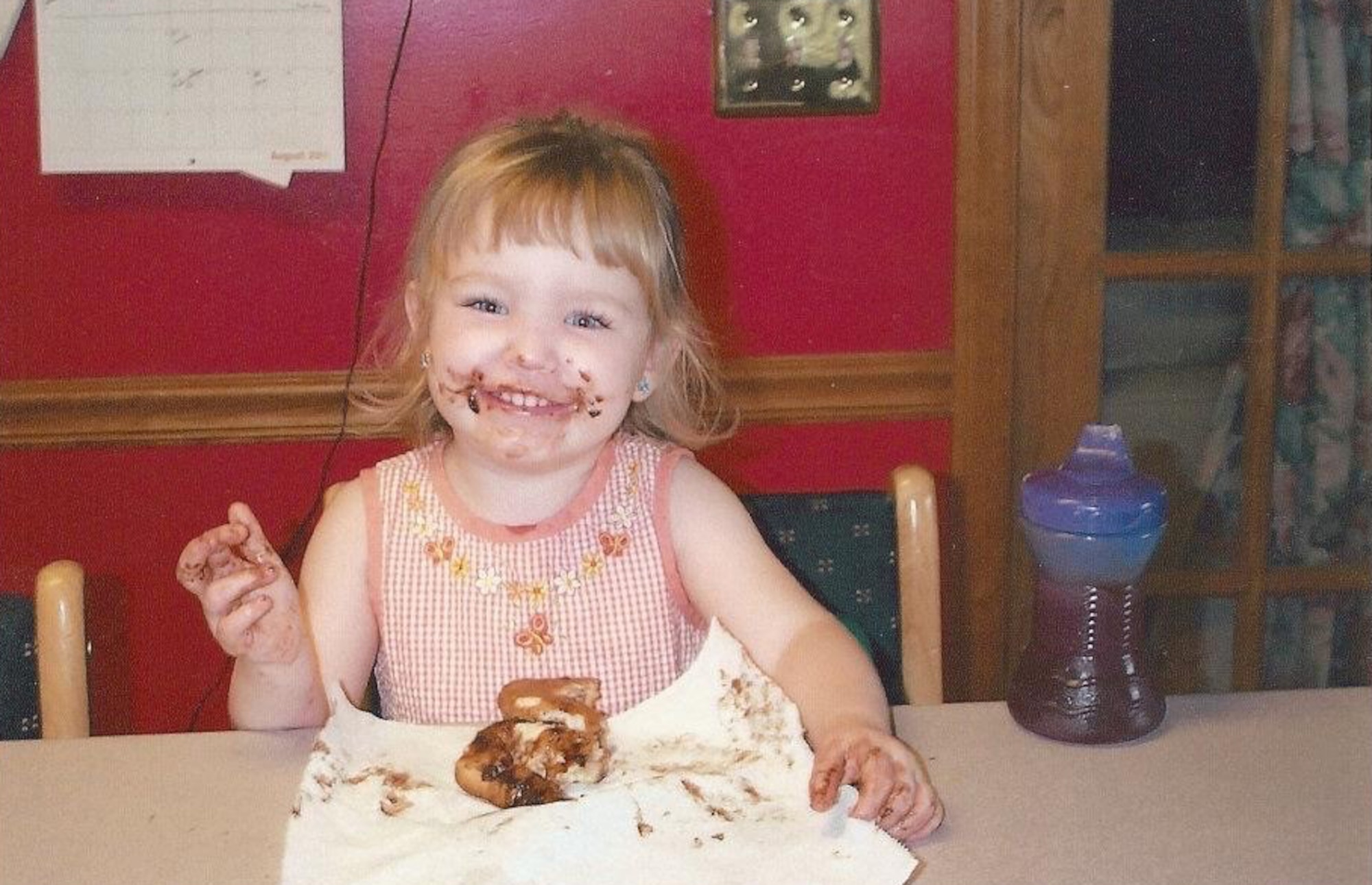 A small girl eats chocolate cake and smiles.