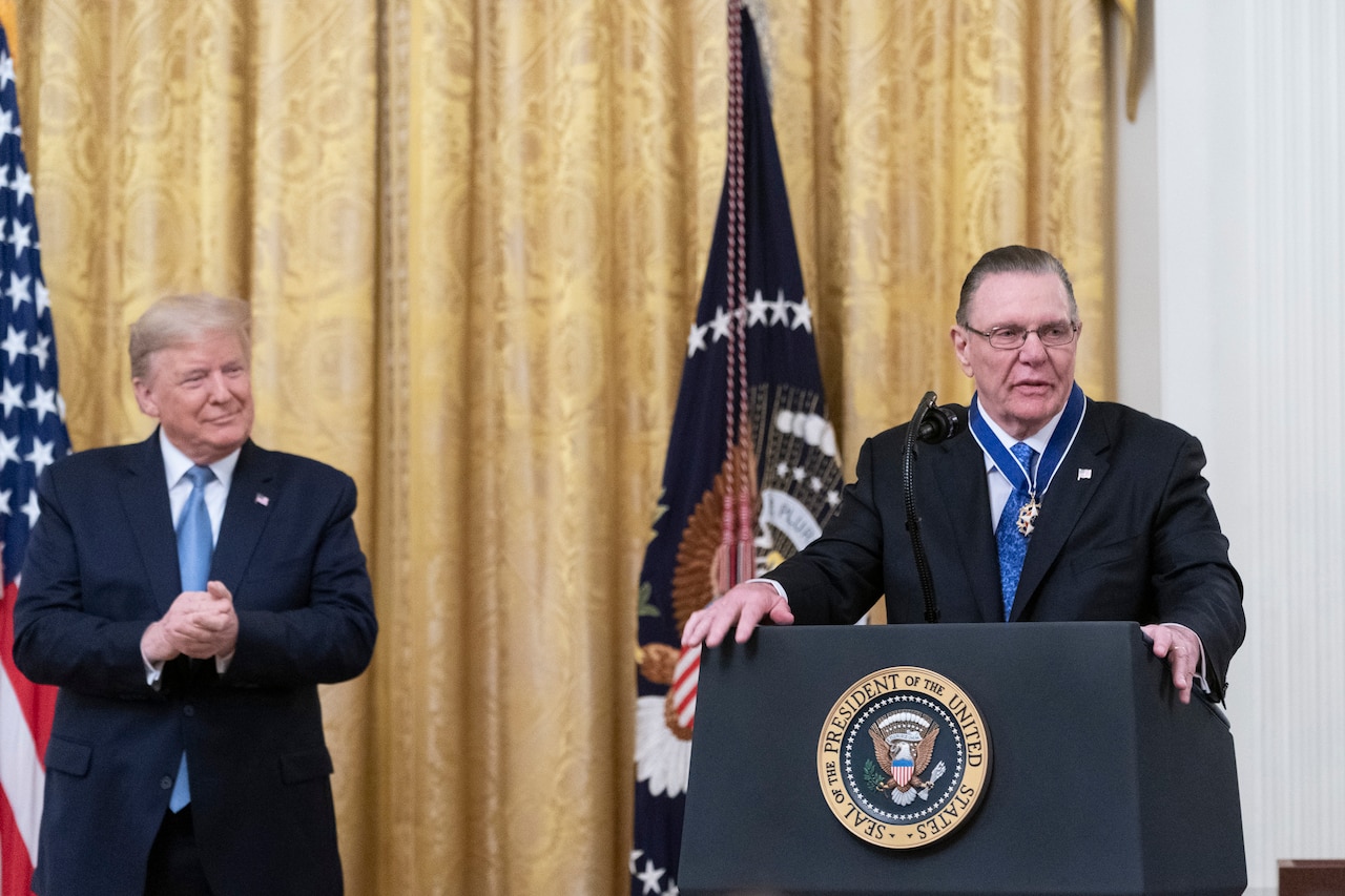 One man speaks from behind a podium while another listens.