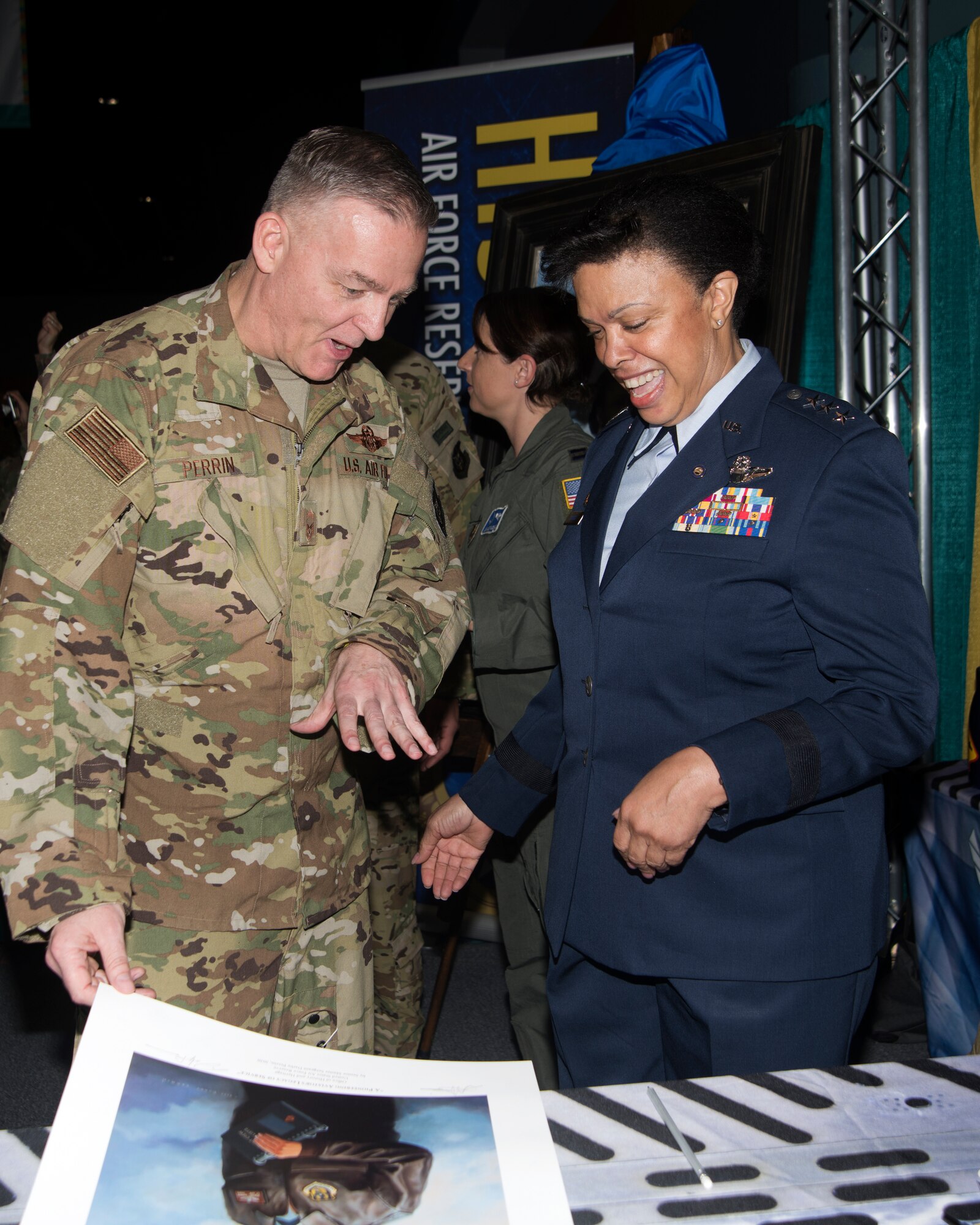 Image of Senior Master Sgt. Darby Perrin, heritage and combat artist and  Lt. Gen. Stayce Harris (retired) look at prints of the recently unveiled a painting a portrait of Harris during the 2020 Women in Aviation Conference, March 6 in Orlando, Florida. The portrait shows Harris standing in a flight jacket with flight crew checklists in hand with a KC-135R and C-141-B flying overhead, both aircraft were flown by Harris. (U.S. Air Force photo by Staff. Sgt. Cierra Presentado)