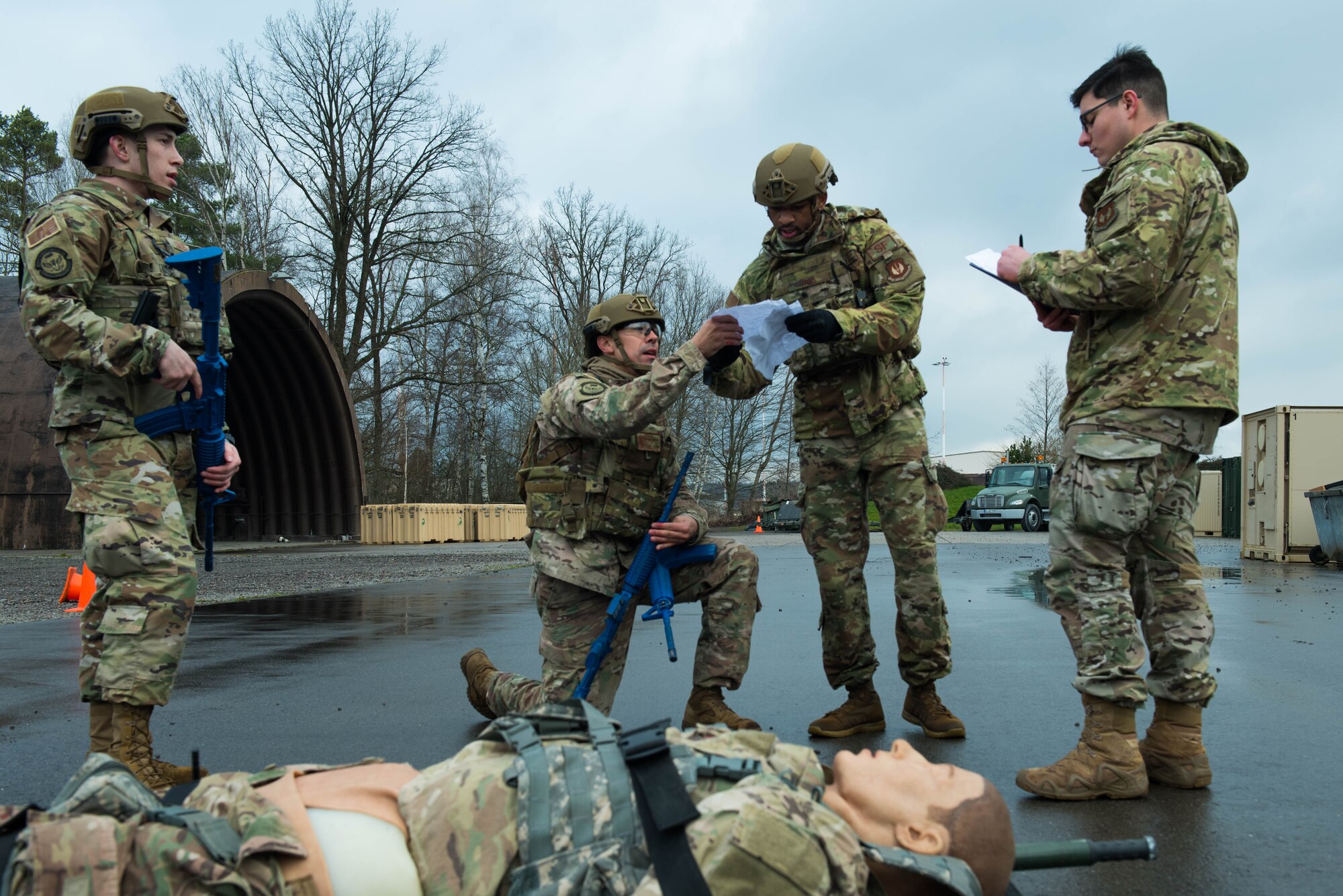 A U.S. Air Force group of security forces Airmen gather around a simulated injured body and gather information to pass on to the proper authorities.