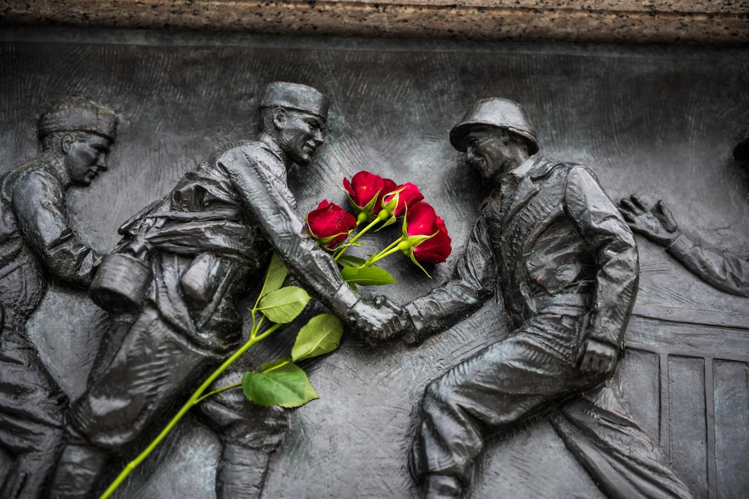 Red roses hang from part of a statue on a memorial.