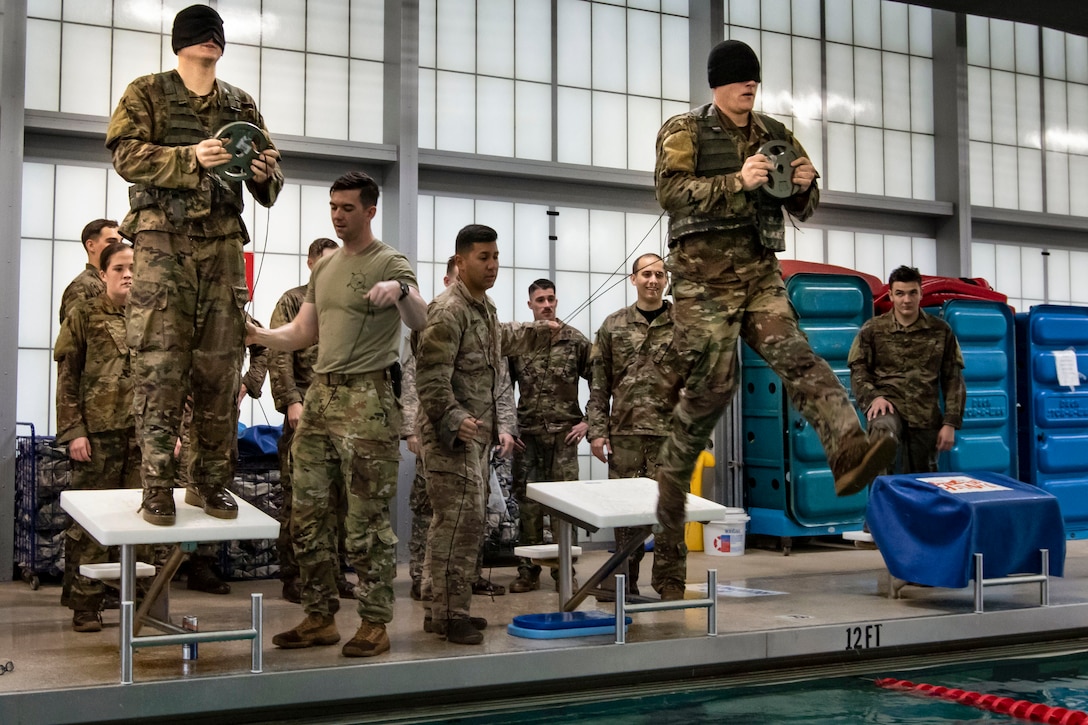 Soldiers jump into a pool while carrying a weights.
