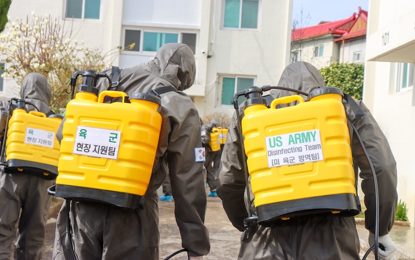 People in chemical suits spray disinfectant.