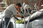 An Aircraft maintainer standing on a platform to conduct maintenance on a T-38 cockpit inside a hangar.