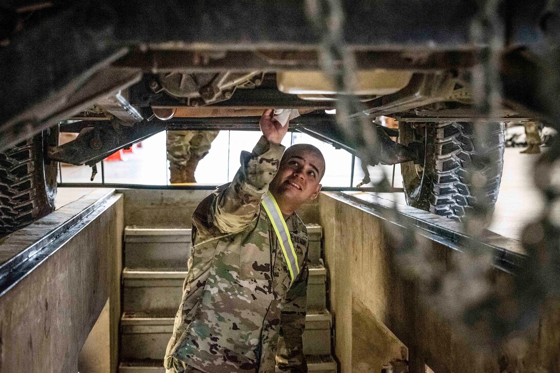 A soldier inspects the undercarriage of a vehicle.