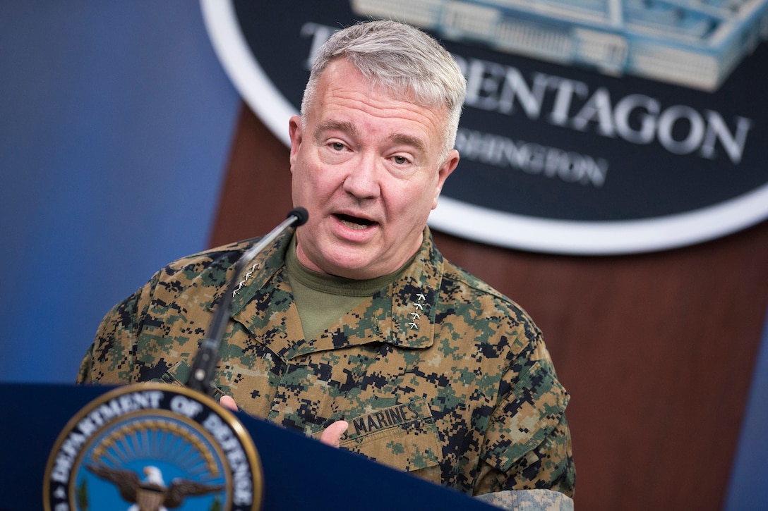 A man in a military uniform stands behind a lectern.