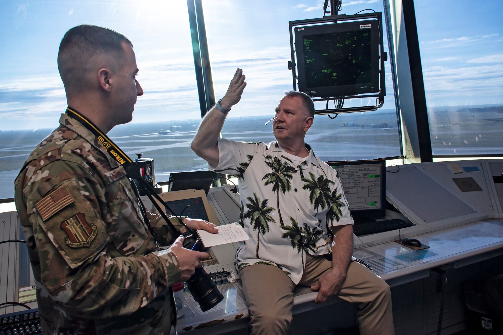 U.S. Air Force Senior Airman Jonathon Carnell, 60th Air Mobility Wing Public Affairs photojournalist, left, listens to Kenneth Breedlove, 60th Operations Support Squadron air traffic controller, explain aspects of tower operations March 11, 2020, at Travis Air Force Base, California. Breedlove also discussed the value of simulation training for air traffic controllers where trainees are allowed the space to fail in a low-threat environment in order to learn best practices. (U.S. Air Force photo by Senior Airman Christian Conrad)
