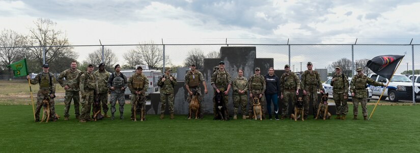 A group of military working dog handlers and their dogs pose for a photo after a ruck march.