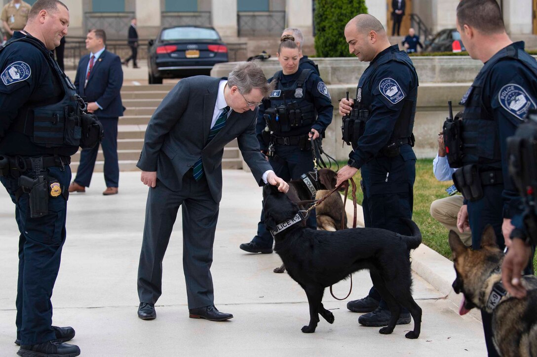 Deputy Defense Secretary David L. Norquist pets a dog; others surround.