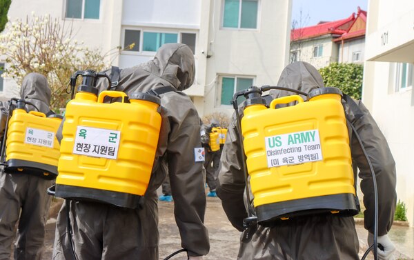 People in chemical suits spray disinfectant.