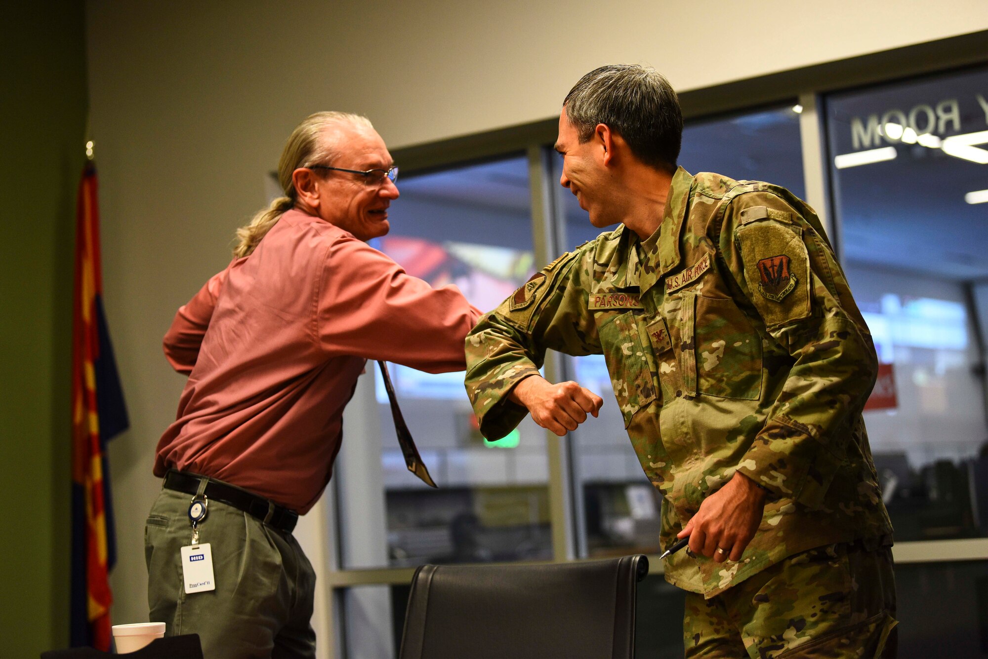 A photo of an airman and a civilian sharing an elbow "high-five"