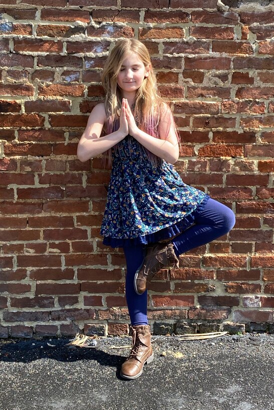 A girl strikes a yoga pose in front of a brick wall.