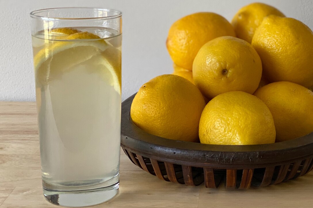 A basket of lemons sits beside a glass of lemonade.