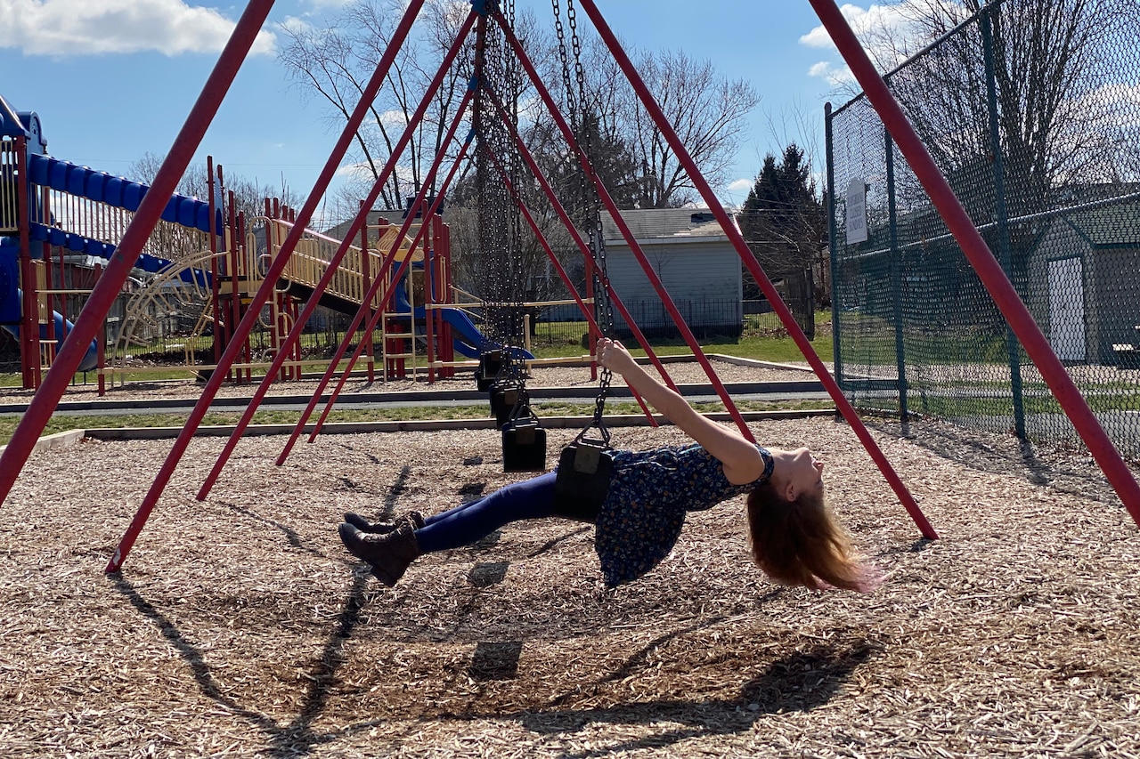 A girl is parallel to the ground while riding a swing at a playground.