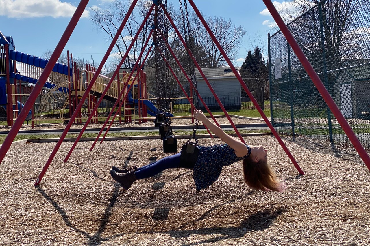 A girl is parallel to the ground while riding a swing at a playground.