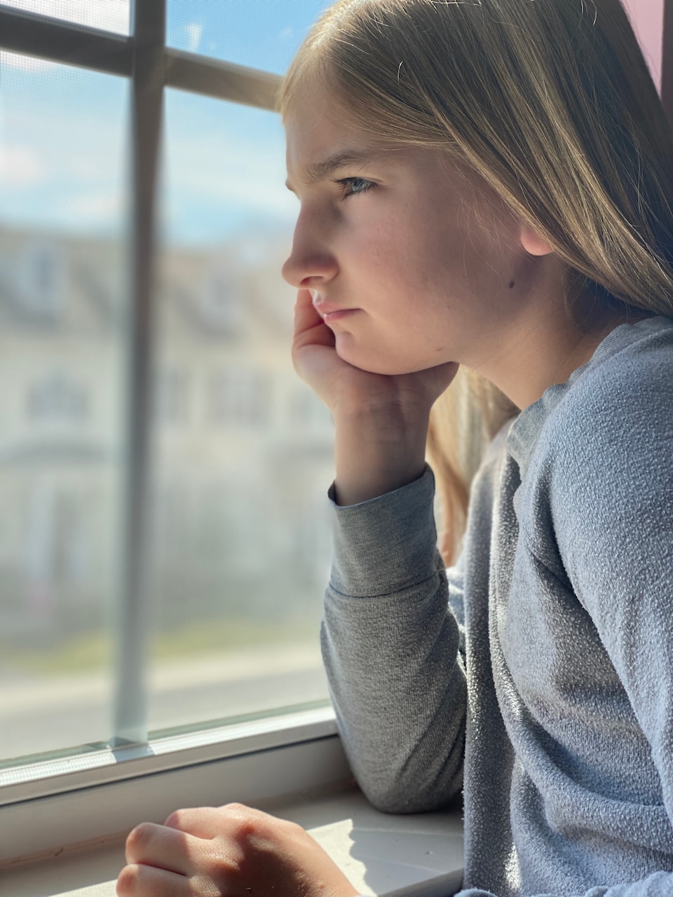 A girl looks out a window wistfully.