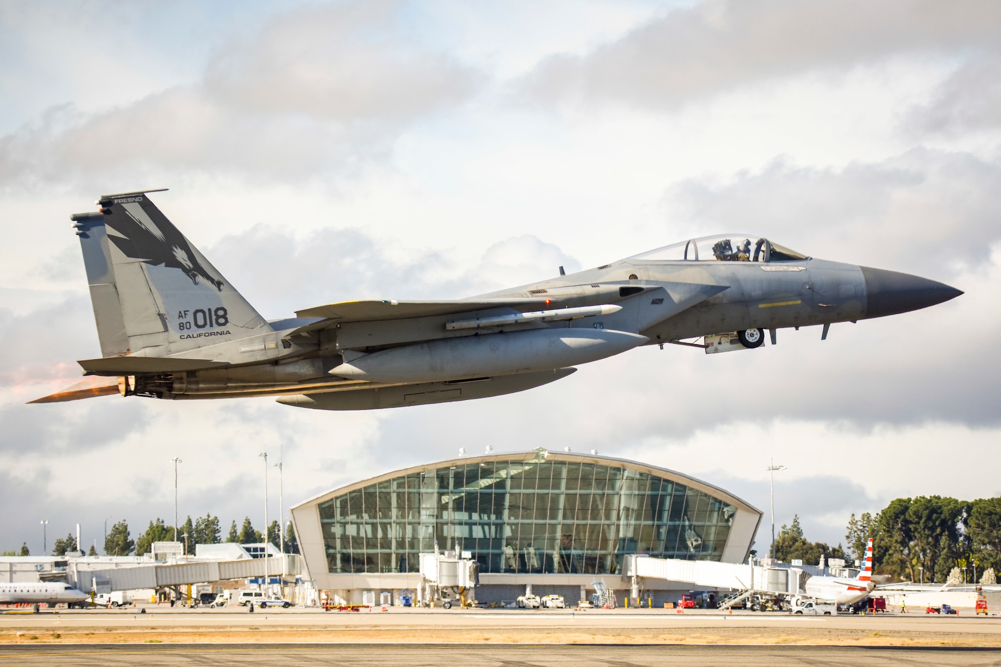 An F-15C Eagle from the 144th Fighter Wing takes off from the Fresno Yosemite International Airport with airport's main terminal in the background, Mar. 17, 2020, to conduct a routine training mission, ensuring pilots maintain required training hours and the Wing maintains mission readiness. (U.S. Air National Guard photo by Capt. Jason Sanchez)