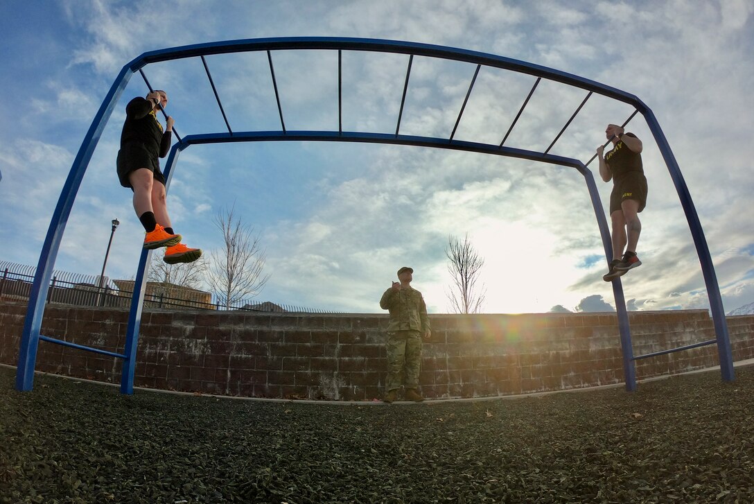 Two soldiers hang from pullup bars as a third watches.