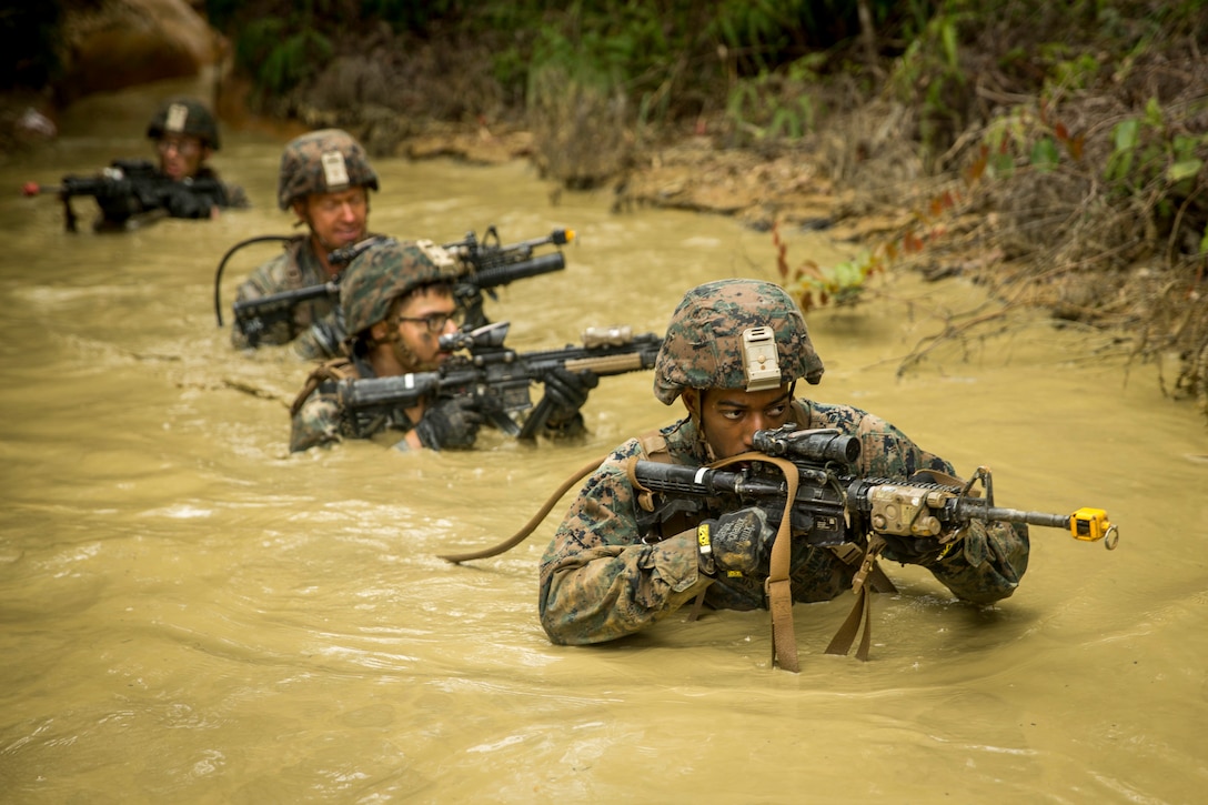 A group of Marines holding weapons wade through muddy water.