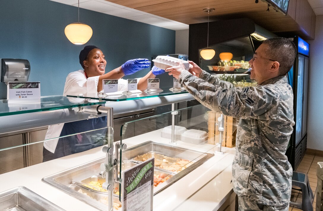Jessica Barlow, 436th Force Support Squadron Sodexo worker, hands Airman 1st Class Nanchun Dong, 736th Aircraft Maintenance Squadron communication and navigation apprentice, his meal in a to-go container March 17, 2020, at the Patterson Dining Facility on Dover Air Force Base, Delaware. All meals are being served to patrons in containers to mitigate the possible transmission of COVID-19. (U.S. Air Force photo by Roland Balik)