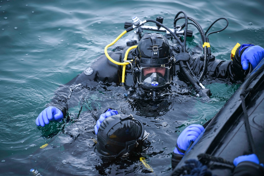 Sailors wearing dive gear move in water up to their shoulders.