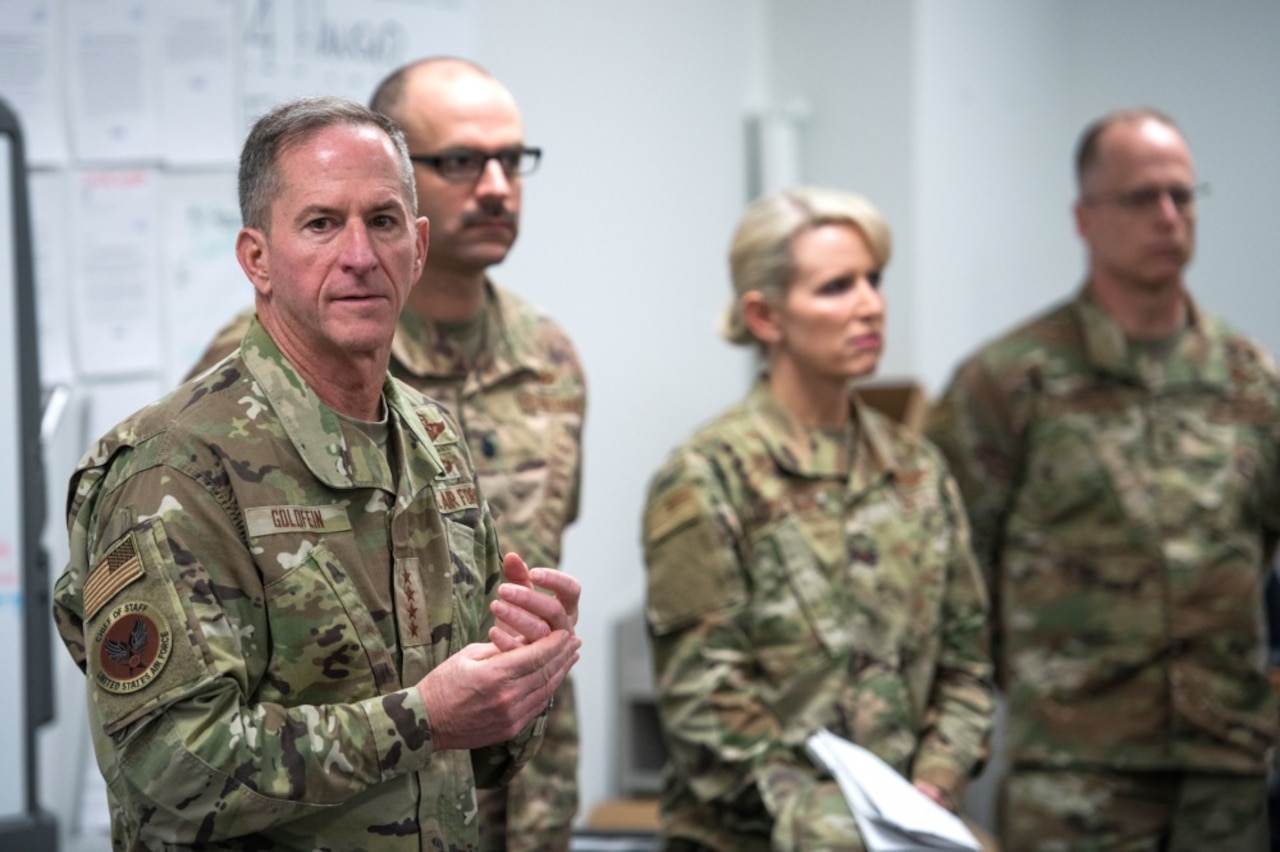 A four-star general stands near other military officers in camouflage uniforms.