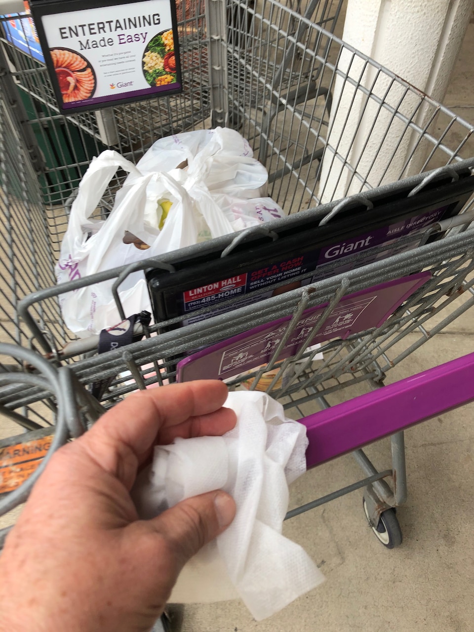 A person’s hand is holding a wipe to clean a shopping cart handle.