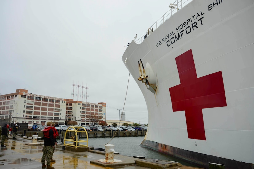 A large white ship is tied to a dock. The ship has the words “U.S. Naval Hospital Ship Comfort” on the side, along with a large red cross.