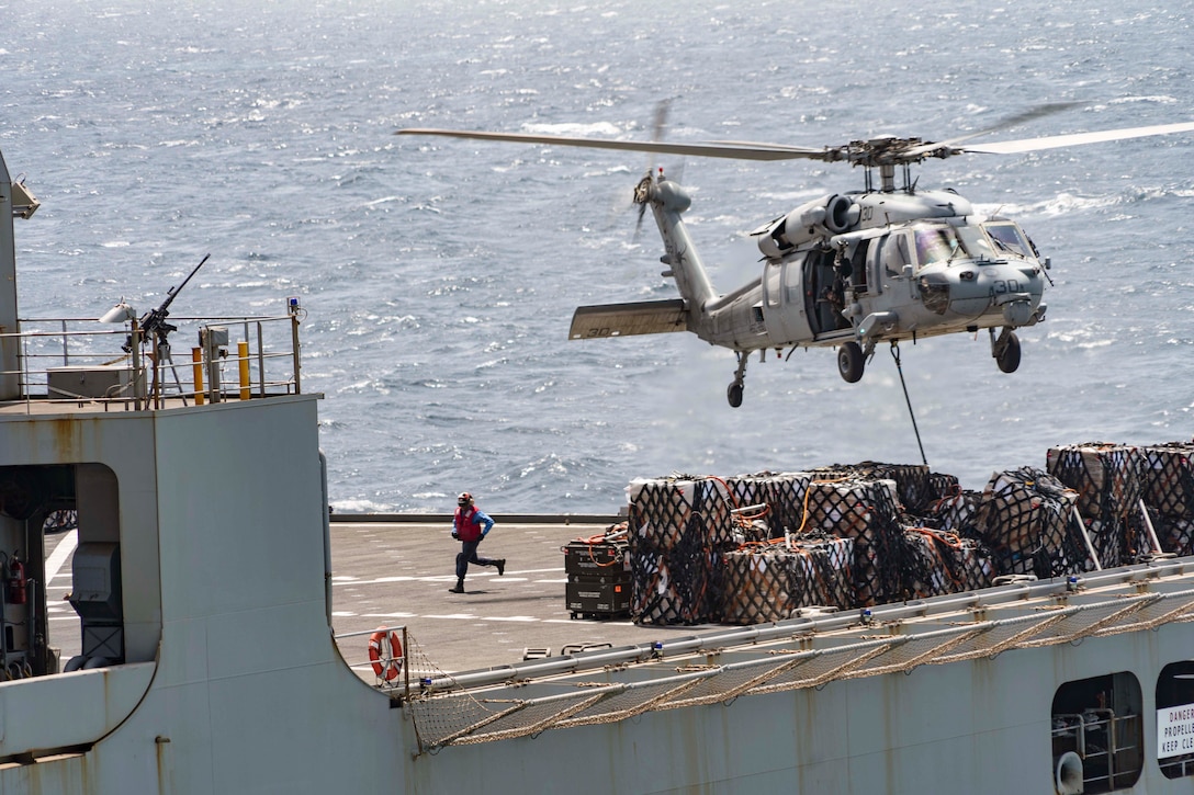 A helicopter hovers over cargo from a ship at sea.