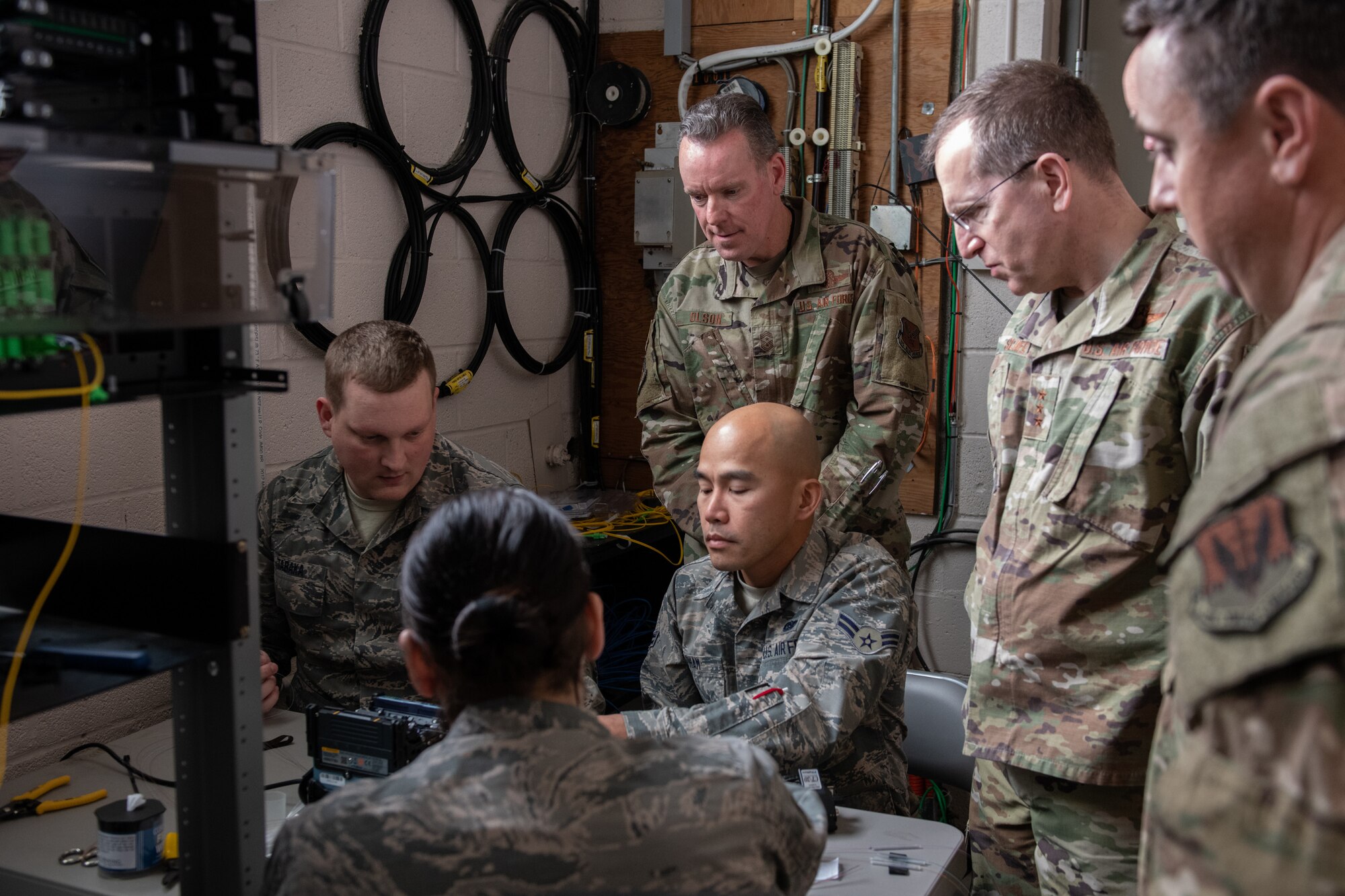 Installation Squadron (205th EIS), delicately splice fiber cable while being observed by U.S. Air Force Lt. Gen. Jim Slife (standing second from right), commander of Air Force Special Operations Command (AFSOC), and Command Chief Master Sgt. Cory M. Olson, AFSOC command chief master sergeant (standing left), during an immersion tour of the 137th Special Operations Wing at Will Rogers Air National Guard Base (WRANGB) in Oklahoma City, March 7, 2020. The 205th EIS is a tenant unit at Will Rogers and provides infrastructure support to the Wing while also fulfilling worldwide taskings and deployments. (U.S. Air National Guard photo by Senior Master Sgt. Andrew M. LaMoreaux)