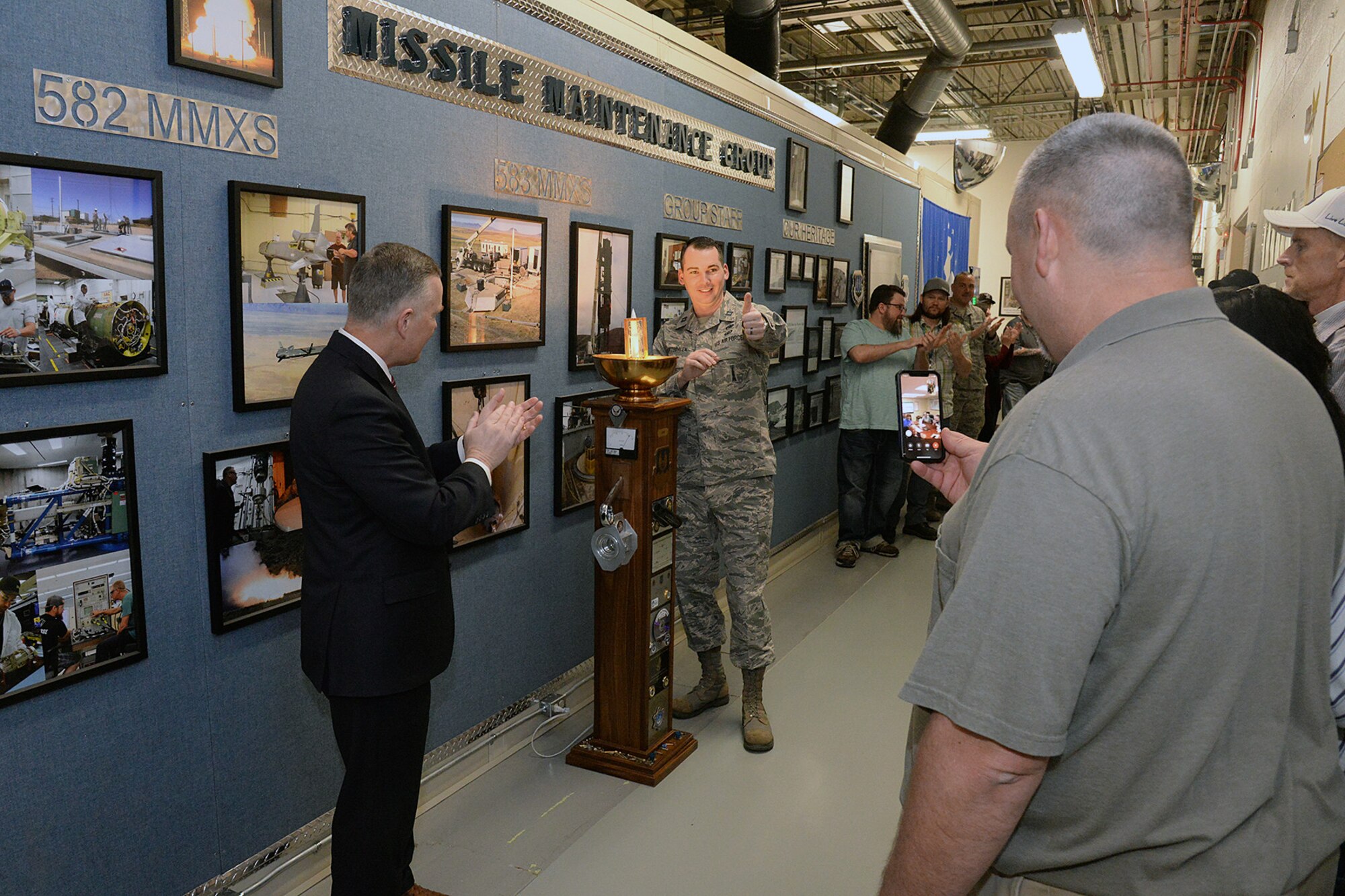 Eric Fox, Ogden Air Logistics Complex vice director, left, and Capt. Ryan VanArtsdalen, 583rd Missile Maintenance Squadron (MMXS) deputy commander, center, applaud the presentation of the LAMP award to members of the 583rd MMXS who attended the ceremony virtually from Malmstrom Air Force Base, Montana, March 11, 2020, at Hill Air Force Base, Utah. The squadron was recognized for its dedication to safety and accomplishing its production under extreme weather conditions. (U.S. Air Force photo by Alex R. Lloyd)
