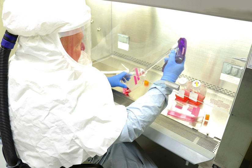 A man in a protective suit puts fluid in a tube.